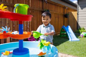Toddler playing with a water table in a backyard daycare setting, ideal for daycare for 2 years old and daycare for 3 year old children.